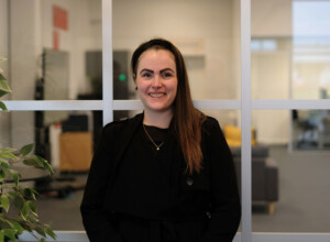 Smilende kvinde med mørkt hår iført sort hårbånd og sort tøj